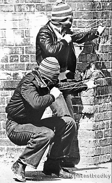 Young hooded men firing catapults, Belfast, Northern Ireland, by Stephen S T Bradley, editorial, commercial, PR and advertising photographer, Dublin, Ireland