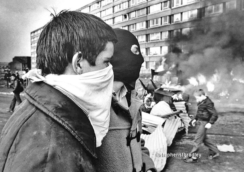Hooded young men beside burning vehicle, Divis Flats, Belfast, by Stephen S T Bradley, editorial, commercial, PR and advertising photographer, Dublin, Ireland